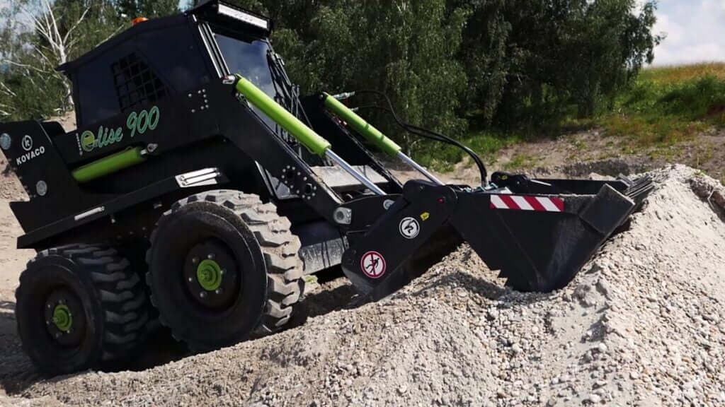Kovaco 4 in 1 Bucket attachment on a skid steer loader working on a gravel pile.