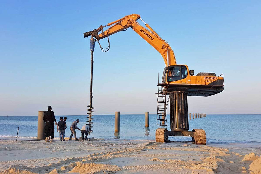 Auger S4- 65mm RND- 1200mm being operated by excavator on beach, demonstrating versatility for construction projects.