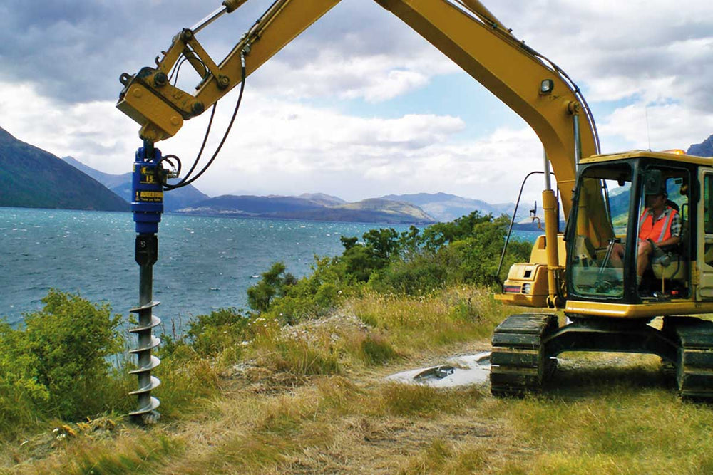 Excavator using Auger S5- 75mm Sq- Length 1500mm by a lakeside for efficient drilling.