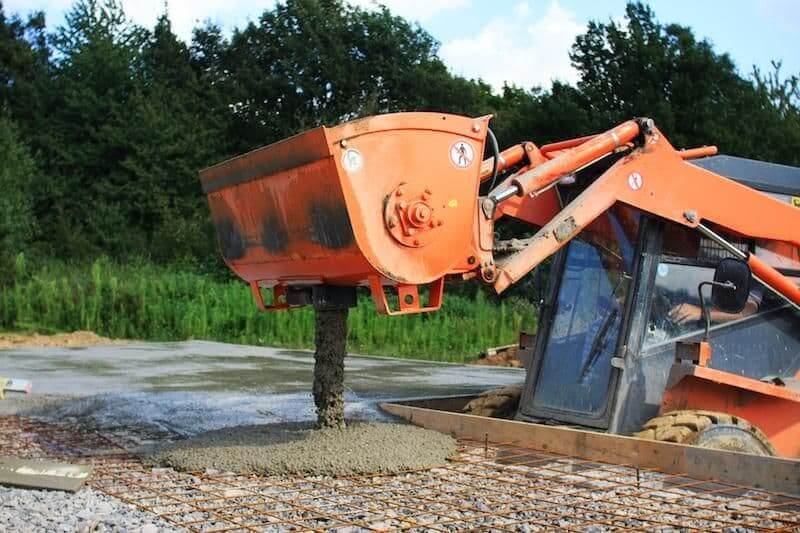 Kovaco - Concrete Mixing Bucket pouring concrete on a construction site with machinery in use.